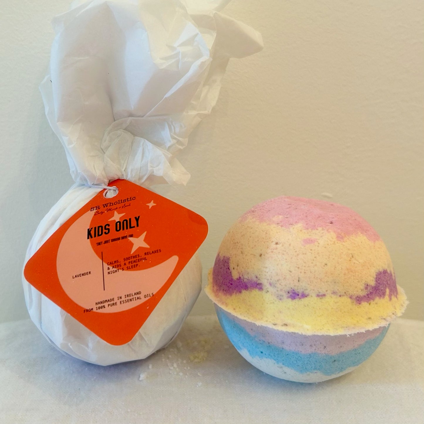 "A brightly colored rainbow Kids Only Bath Bomb with a white tag displaying the product name; made with 100% natural ingredients and gentle lavender essential oil, perfect for sensitive skin & aids a peaceful nights sleep"