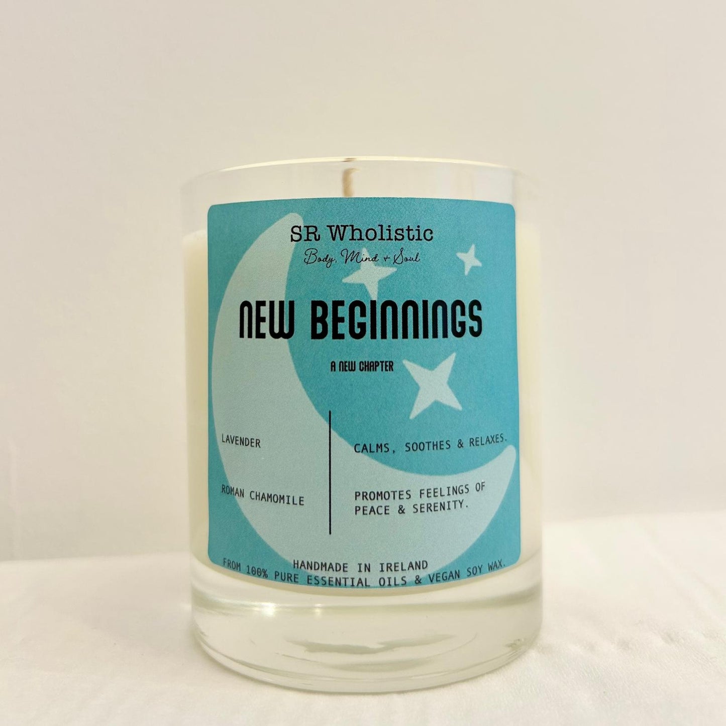 "New Beginnings candle in a clear glass jar with label clearly visible, standing alone on a neutral background."