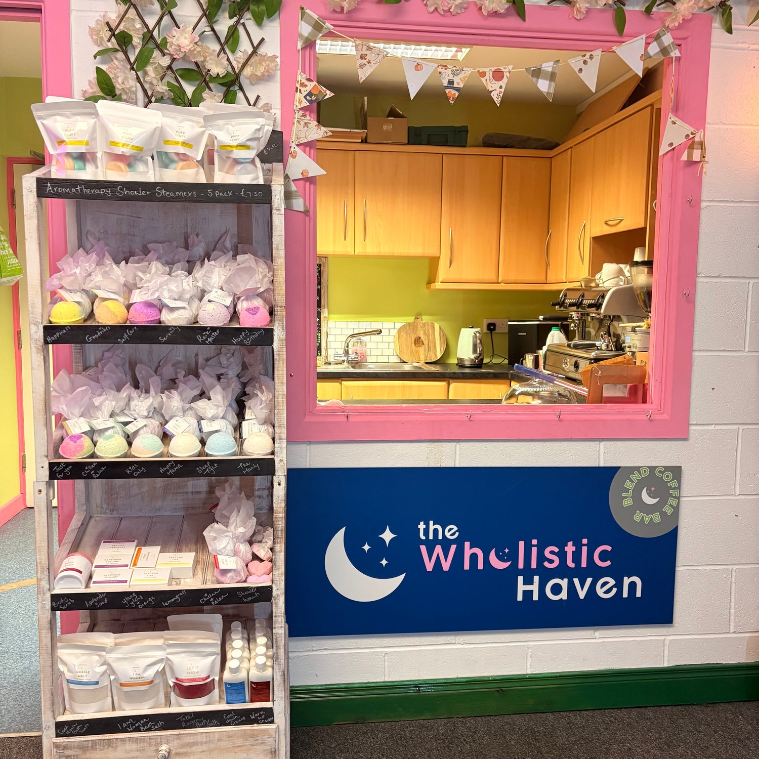 Shelf with products and a pink-framed window into a kitchen, with 'the Whelistic Haven' sign visible.