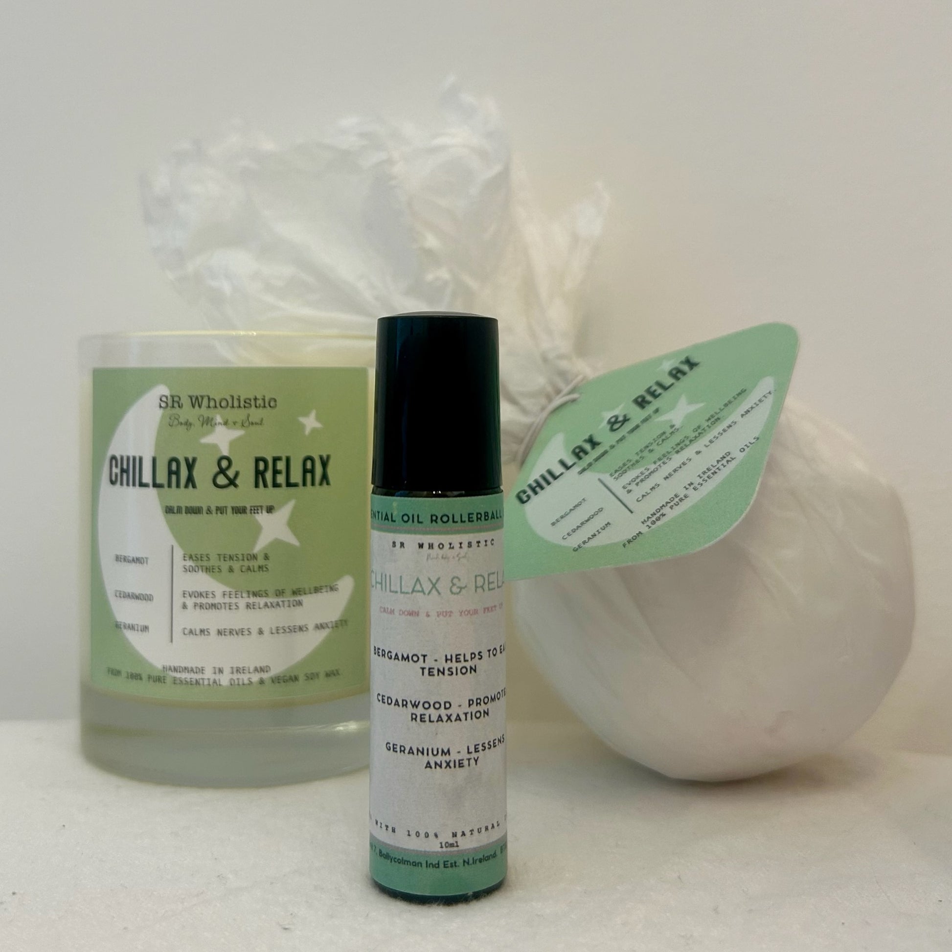 "Chillax & Relax candle, bath bomb, and essential oil rollerball set in a calming flat lay – handcrafted with grounding cedarwood, uplifting bergamot, and balancing geranium."