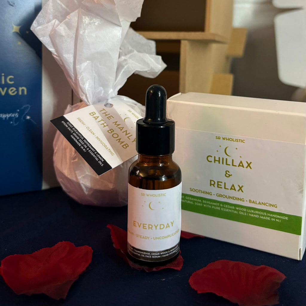 Bottle of 'Everyday face serum' oil with a dropper, bath bomb, and 'Chillax & Relax' Soap on a dark surface.