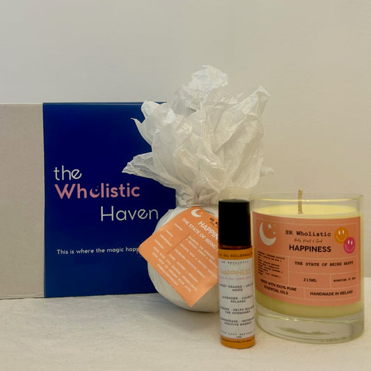 "Happiness Gift Set displayed beside its cheerful gift box, featuring a mood-boosting trio of candle, bath bomb, and rollerball with essential oils of jasmine, lemongrass, lavender, and orange."