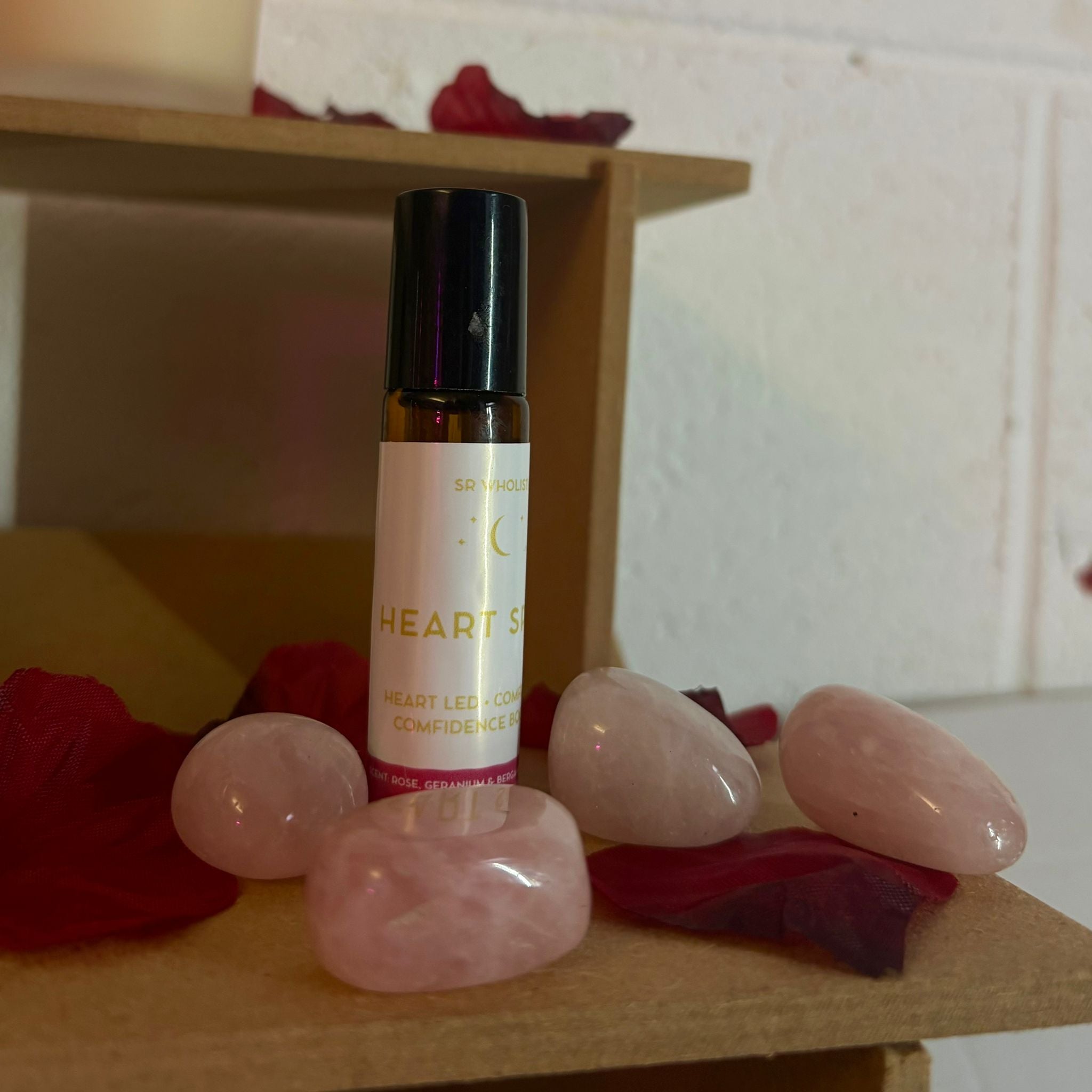 Roller bottle labeled 'Heart's Space' with Rose quartz crystals and rose petals on a wooden surface.