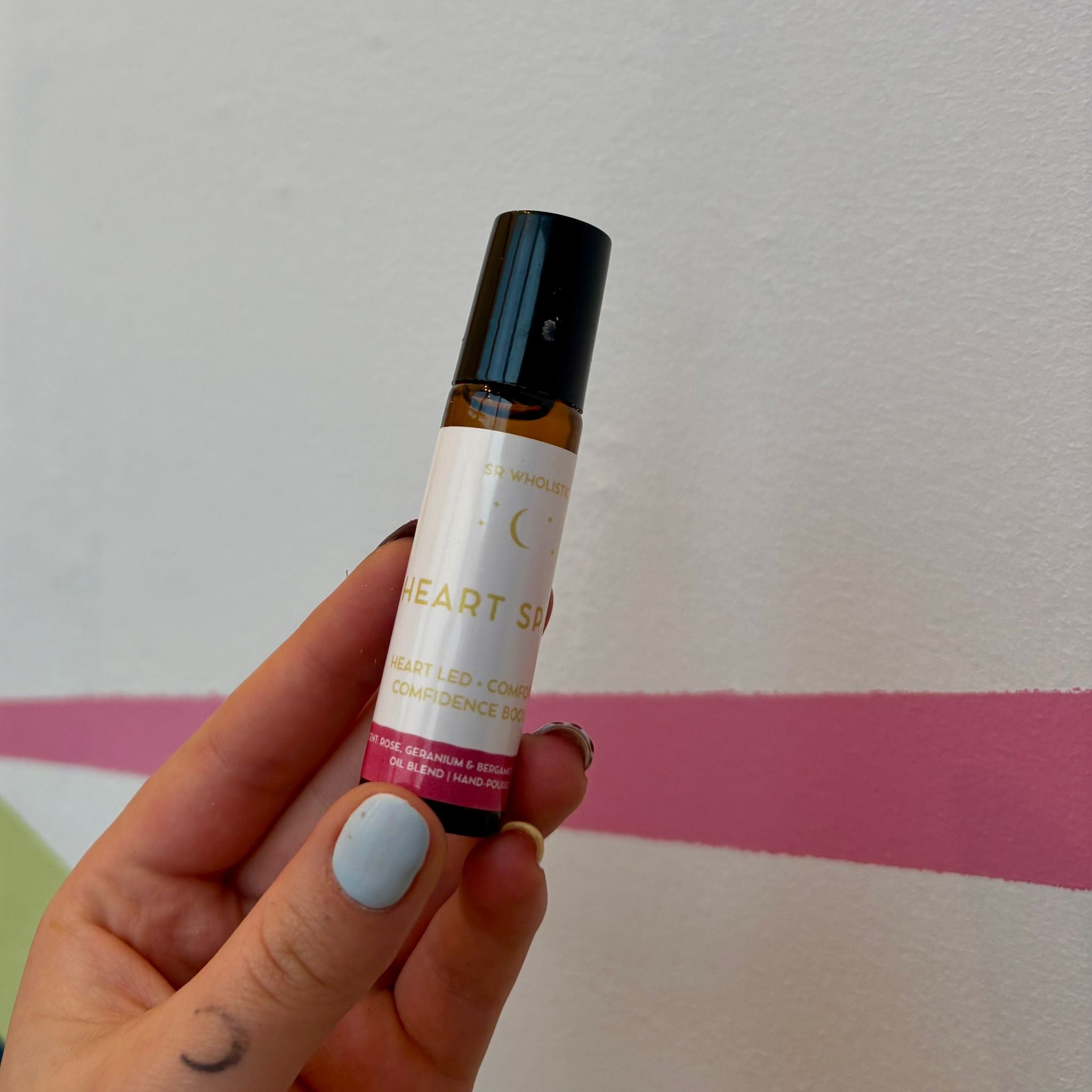 Hand holding a small rollerball bottle labeled 'Heart Space' against a plain background