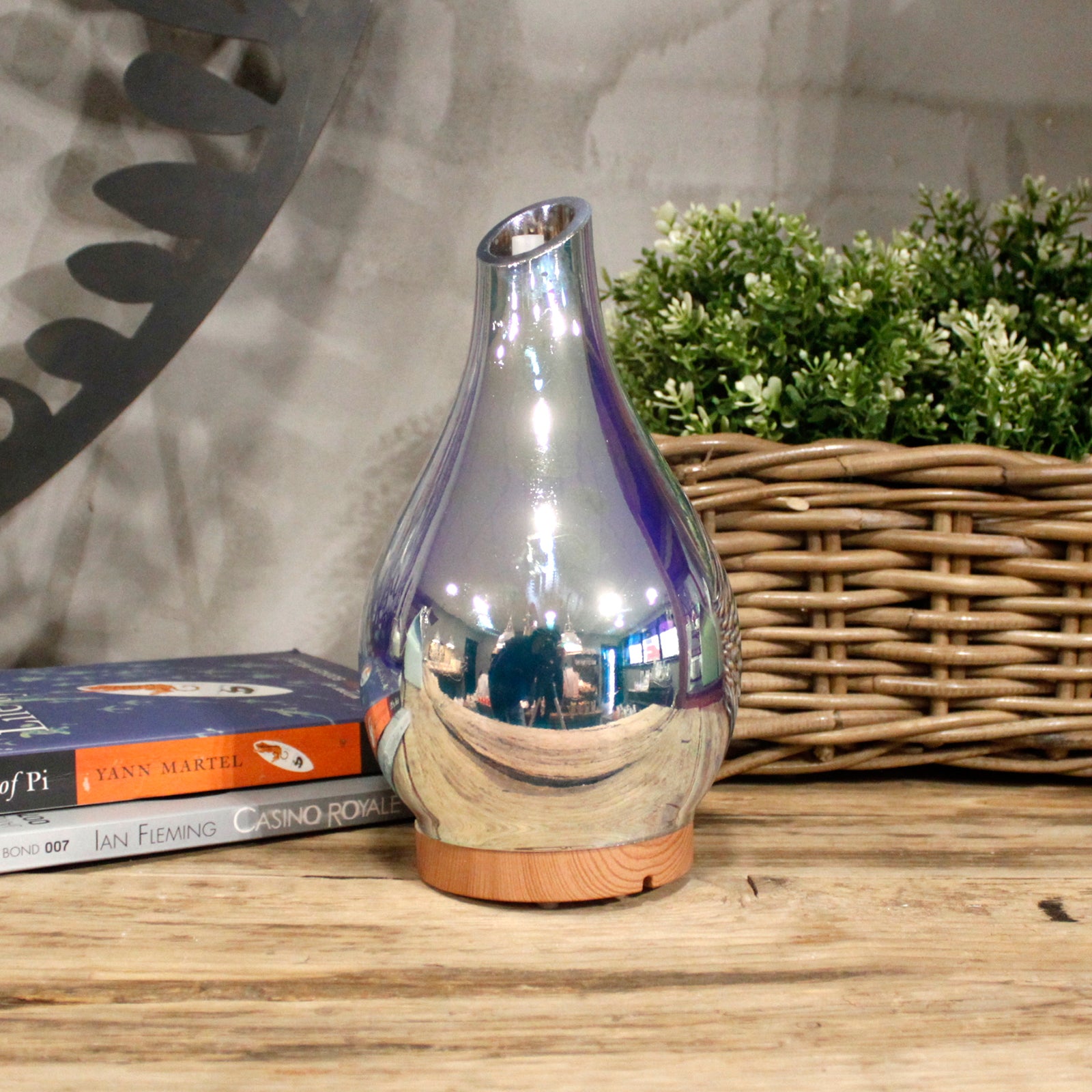 Silver reflective vase on a wooden surface with books and a basket in the background