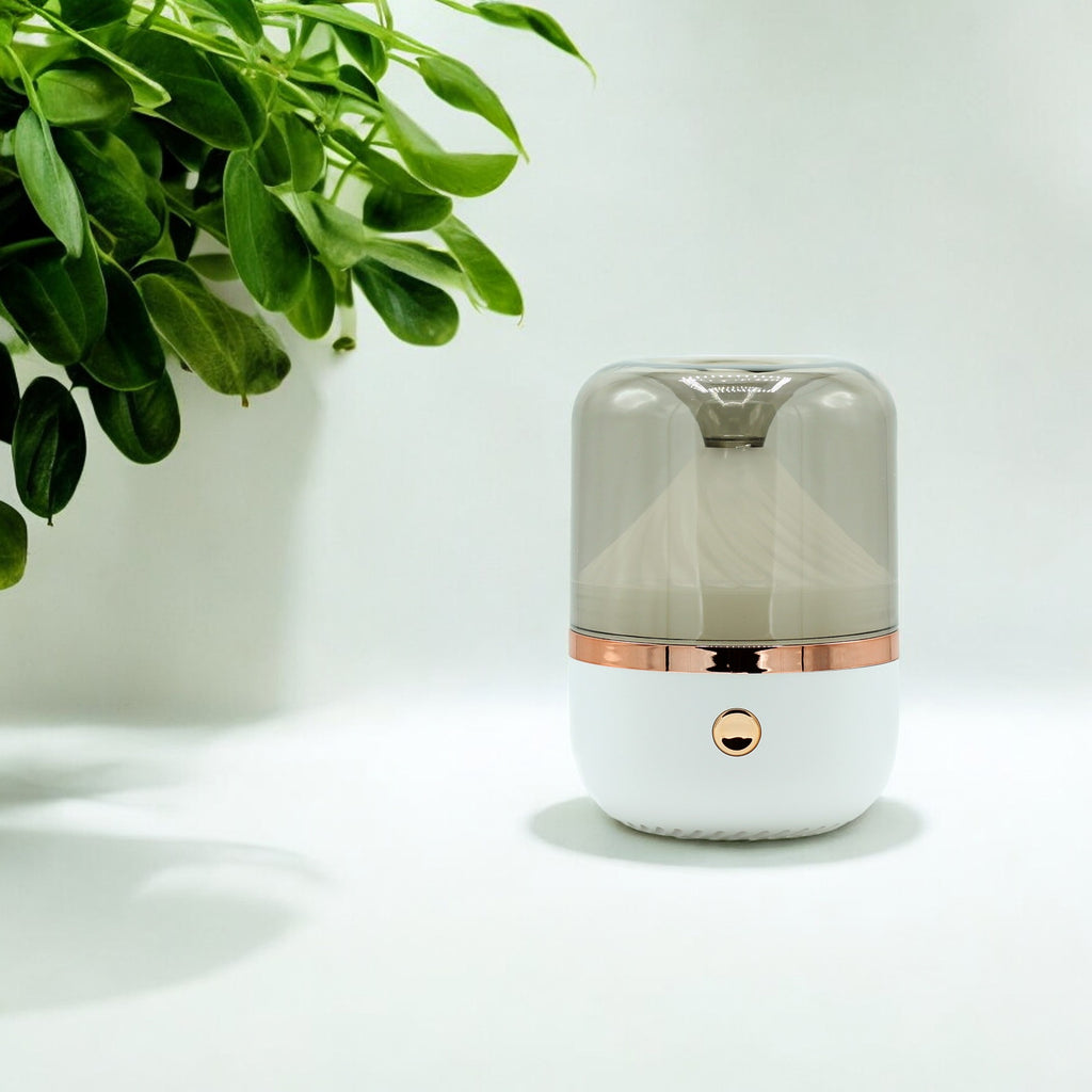 Small cylindrical humidifier with rose gold accents on a light surface with a plant in the corner.