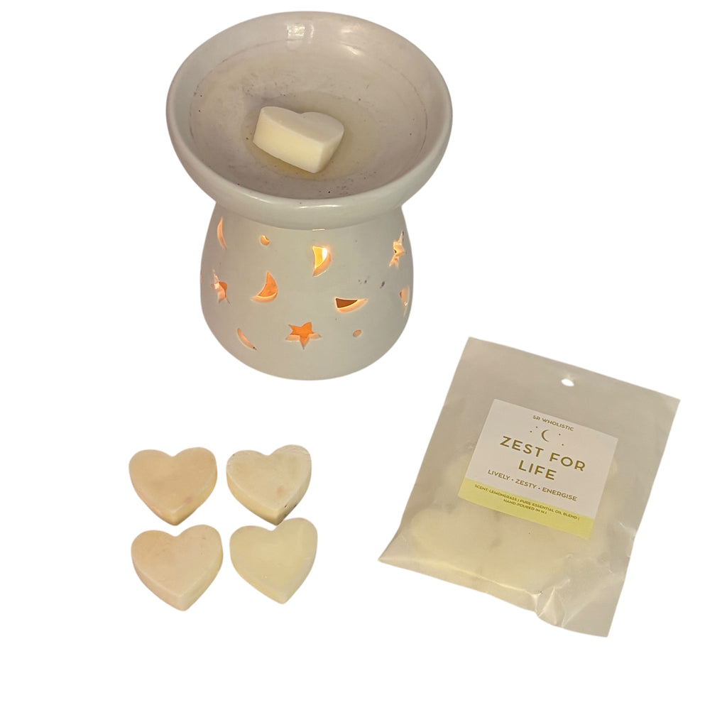 “White ceramic wax burner glowing with warm light, with a heart-shaped wax melt on top, four matching heart melts beside it, and a SR Wholistic ‘Zest For Life’ wax melt pack on a clean white background.”