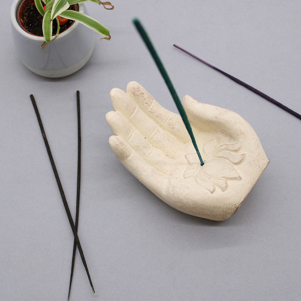 Ceramic hand-shaped incense holder with incense sticks on a light gray background