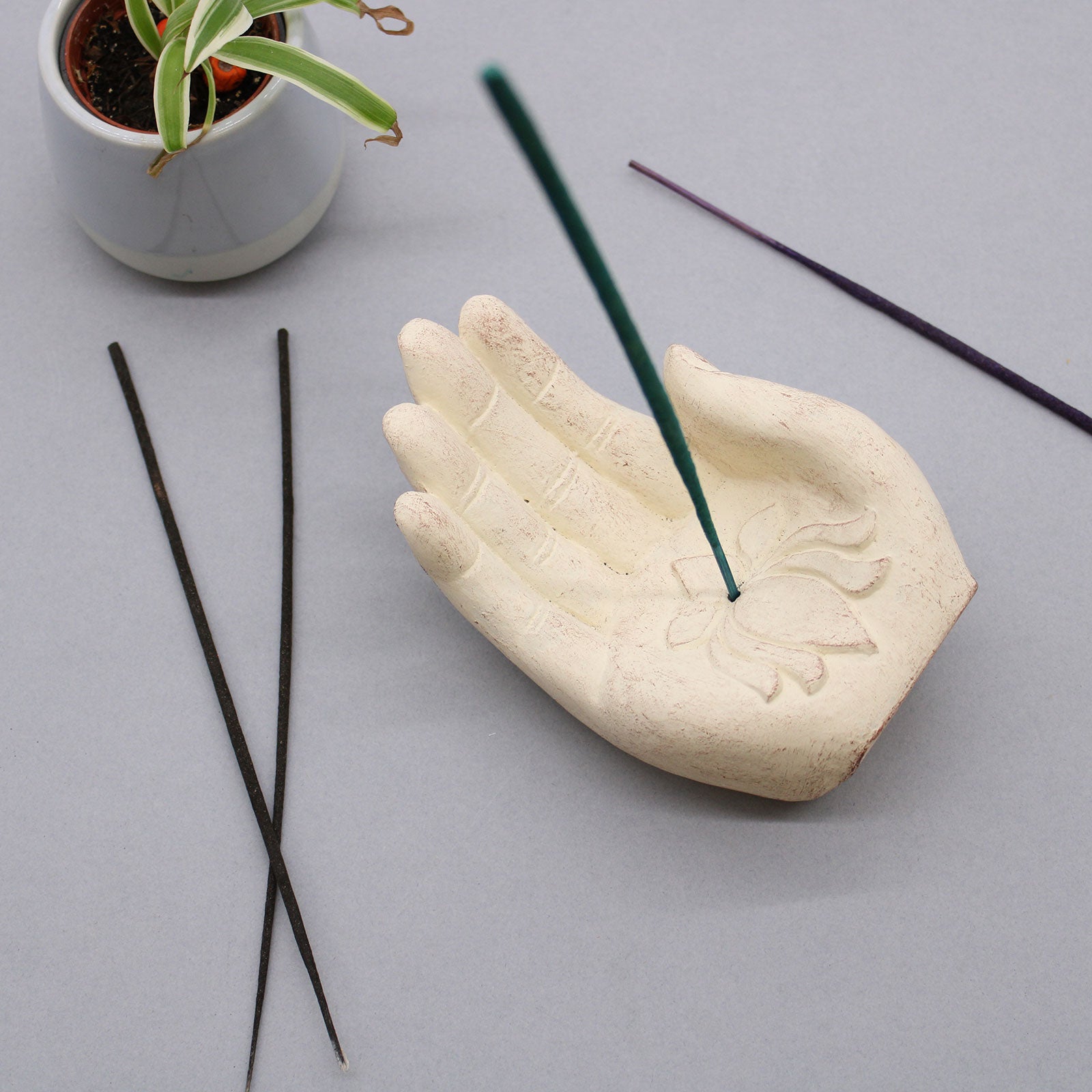 Ceramic hand-shaped incense holder with incense sticks on a light gray background