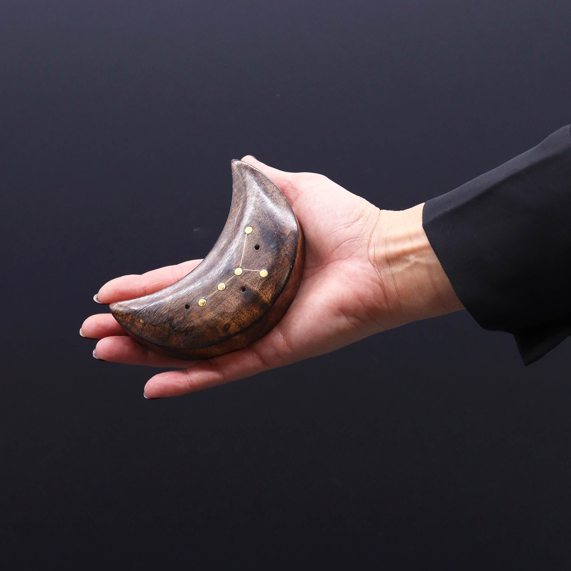 Hand holding a crescent-shaped wooden object with gold accents against a black background